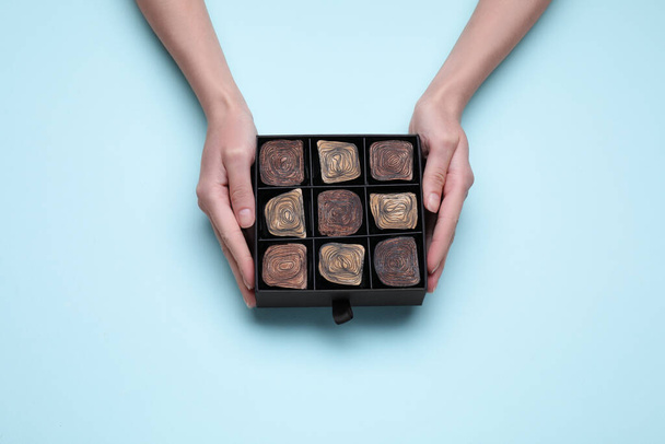 Woman with box of delicious chocolate candies on light blue background, top view - Photo, image