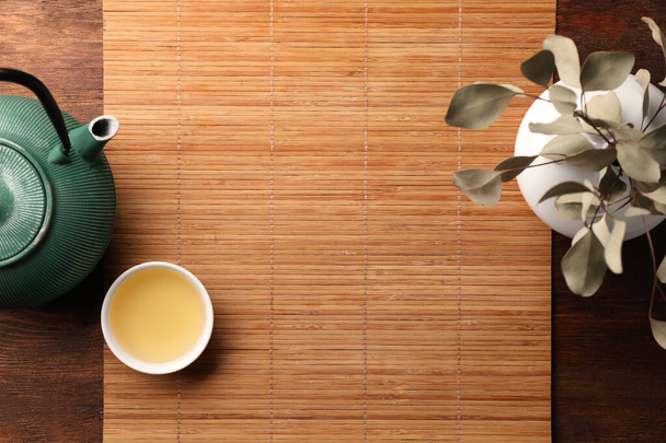 Bamboo mat, teapot, cup of tea and vase with plant on wooden table, flat lay. Space for text - Fotoğraf, Görsel