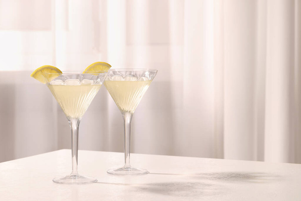 Elegant martini glasses with fresh cocktail and lemon slices on white table indoors. Space for text - Zdjęcie, obraz