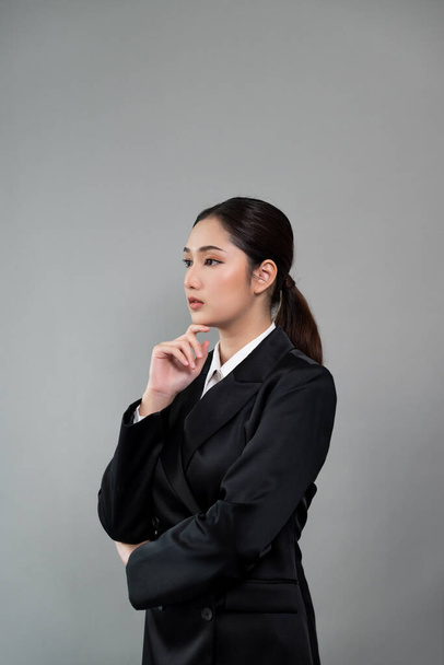 Une jeune femme d'affaires confiante se tient sur un fond isolé, posant en costume noir formel. Dame de bureau ou gestionnaire avec une apparence intelligente et professionnelle. Enthousiaste - Photo, image