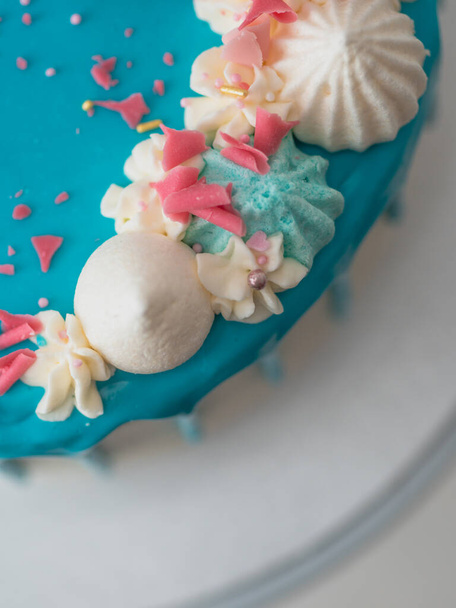studio shot van chocolade mat blauw druppelde glazuur witte beker taart, eenhoorn, meringue en hagelslag op de top - Foto, afbeelding