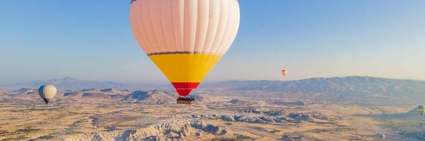 BANNER, LONG FORMAT Colorful hot air balloons flying over at fairy chimneys valley in Nevsehir, Goreme, Cappadocia Turkey. Spectacular panoramic drone view of the underground city and ballooning - Foto, Imagem