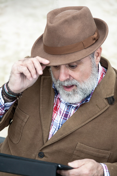 Attractive old man with beard and hat with a tablet - Foto, Imagen