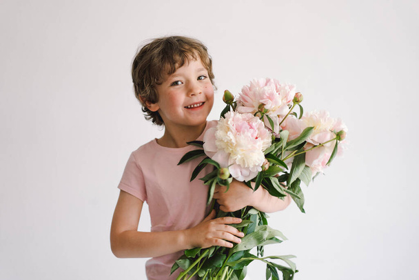 牡丹の花束を持つ陽気な幸せな子供。白地に笑顔の男の子。母の日。愛とロマンチックな概念 - 写真・画像