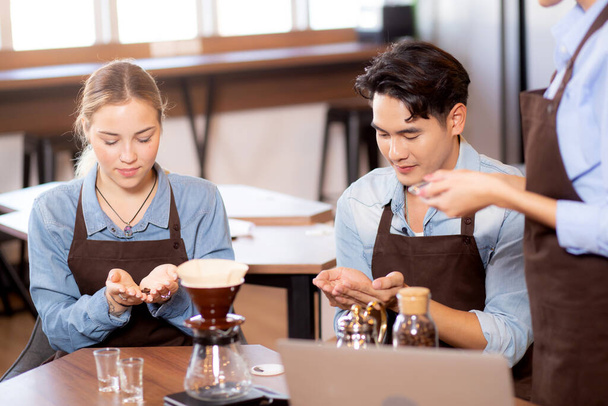 Νεαρός άνδρας και γυναίκα μαθαίνουν να φτιάχνουν καφέ και να μυρίζουν φασόλια με barista ενώ το laptop είναι στο γραφείο στο cafe, ομάδα ανθρώπων που εκπαιδεύουν καφέ στάγδην με επιχειρηματία, μικρή επιχείρηση ή ΜΜΕ. - Φωτογραφία, εικόνα