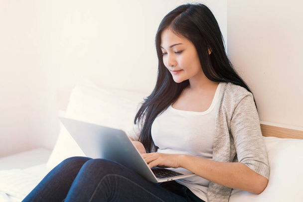 Mujer joven trabajando en una computadora portátil sentada en la cama en casa
. - Foto, Imagen
