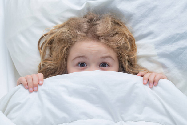 Nightmare kids, child hiding under white blanket, top view. Scared boy hiding in bed. Kid under covers, face cover with blanket. Morning awakening little child in bed. Kid wakes up in the bedroom - Fotoğraf, Görsel