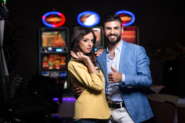 Portrait of a Young Beautiful and Well Dressed Couple Playing in the Casino and Celebrate Showing Thumbs Up and Cross Finger - Zdjęcie, obraz