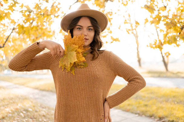 Beautiful girl walking outdoors in autumn. Young woman enjoying autumn weather and collect yellow leaves. Fall concept. Copy space - Photo, image