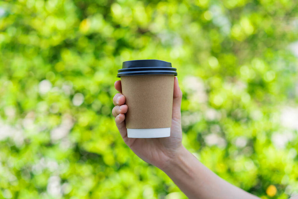 Young male hand holding a coffee paper cup isolated on green nature background - Photo, Image