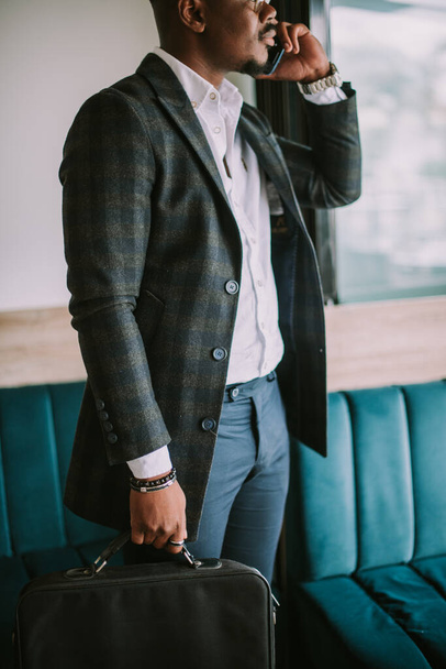 Detalhes de homem de negócios bonito de pé com sua mala e falando em seu telefone - Foto, Imagem