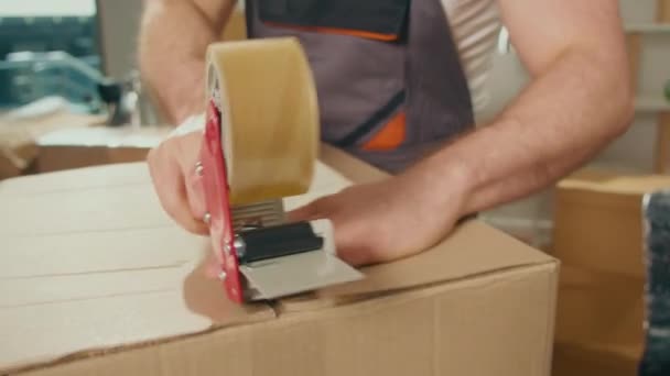 Close-Up of Employee Worker Sealing Cardboard Box Using Duct Tape Machine. Servicios profesionales de embalaje y desembalaje. Embalaje y preparación para el movimiento. Suministros y materiales de embalaje - Imágenes, Vídeo