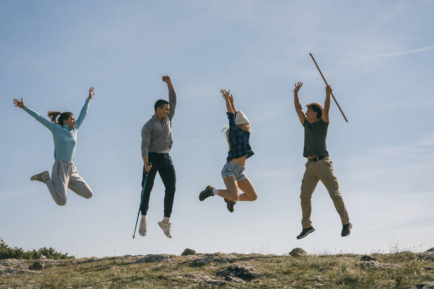 Молодые туристы на вершине горы веселятся. Они счастливы и прыгают. - Фото, изображение