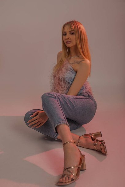 Vertical seductive, confident, modern, attractive blonde woman with hair bangs in casual clothes posing to camera in pink dark studio. Shopping sales, new boots and shoes collection. Luxury outfit - Photo, Image
