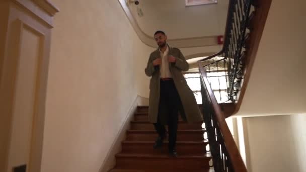 Ein Mann aus dem Nahen Osten mit Jacke verlässt das Gebäude. Person, die eine Holztreppe hinuntersteigt. Selbstbewusster Typ in Bewegung - Filmmaterial, Video