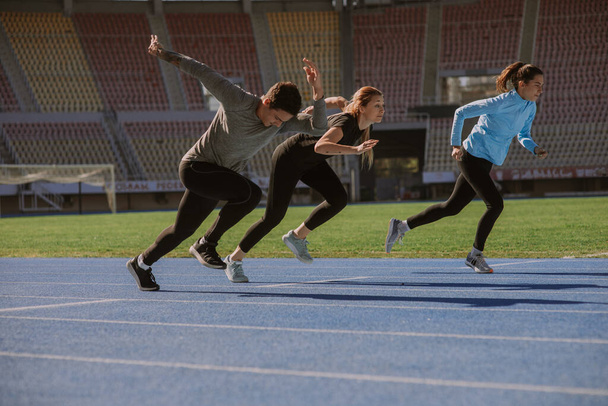 Urheilulliset ystävät treenaavat sydäntä tyhjällä stadionilla aurinkoisena päivänä - Valokuva, kuva
