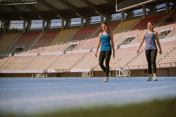 Two pretty girls are done with jogging around the stadium. They are walking on the sports track - Foto, afbeelding