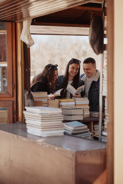 Kitapçıda durup kitap tutarken üç yakın arkadaş gülüyor. - Fotoğraf, Görsel
