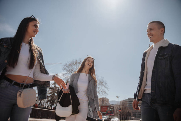 Tre amici intimi ridono insieme mentre camminano nel centro della città - Foto, immagini