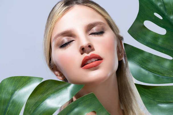 Closeup woman with perfect clean skin and alluring flawless natural soft facial makeup holding green leave monstera. Natural skincare treatment beauty or spa concept in isolated background. - Zdjęcie, obraz