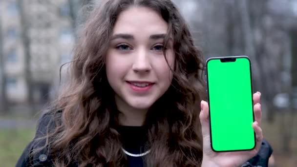 Young woman holds smartphone with green screen index finger showing swipe gesture to copy space to advertise your products on blue background. Ad concept promotional offers - Footage, Video