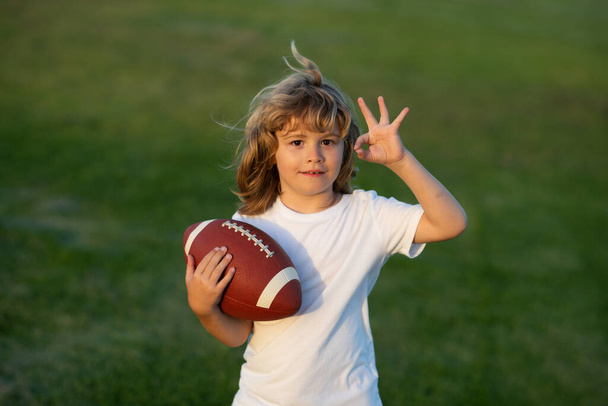 American football. Kid boy playing with rugby ball in park. Child ready to throw a football. Sport kids concept. Sport activities for children outdoors - Foto, Imagem
