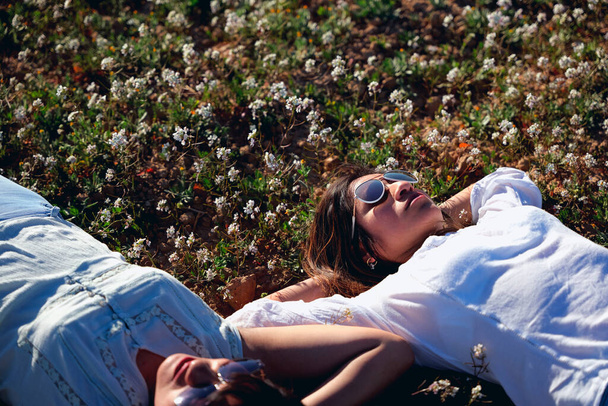 Kaksi naista makaa kukkapellolla kädet pään takana merkkinä rentoutumisesta.. - Valokuva, kuva