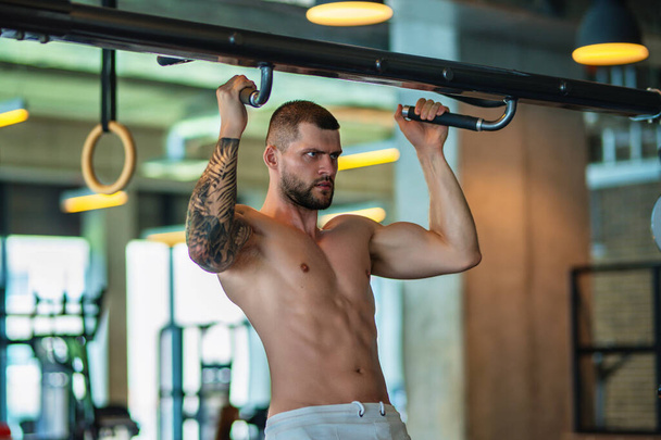 Muscular hunk with posing in gym. Fitness male model near gym equipment. Young muscular man workout. Sport man with strong muscular torso in gym. Sport and motivation. Exercises with weight - Фото, зображення