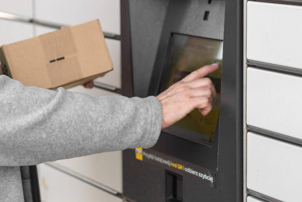 Pniewy, Polonya - 22 Mart 2023. Yaşlı kadınların el kodlarını açıp bir paket göndermek için posta kutusuna el koyuyorlar. E-ticaret nakliyat ve teslimat konsepti. Modern teknoloji. - Fotoğraf, Görsel