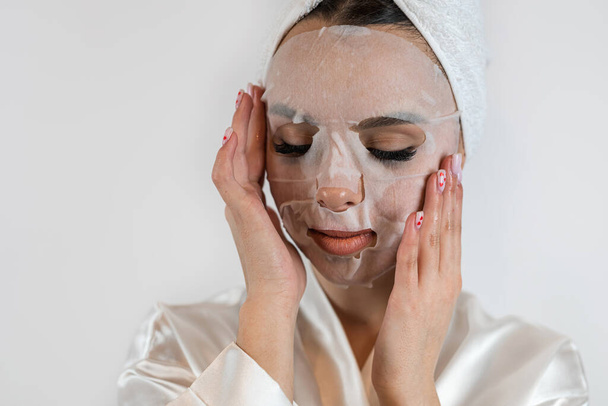 Pretty lady applying moisturizing and tightening mask isolated on white. Spa treatments and skin care    - Фото, изображение