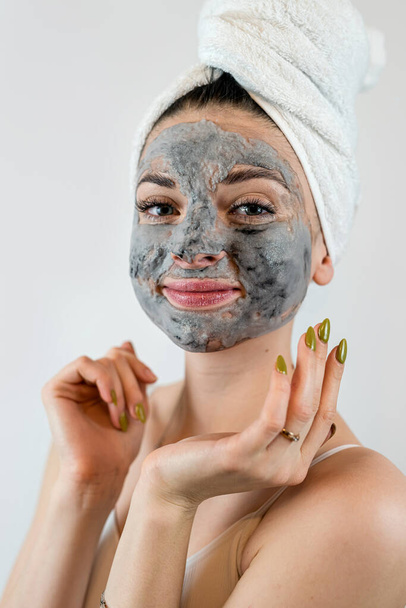 Mujer joven en toalla blanca aplicando máscara de barro negro en su cara aislada en blanco, tratamientos de spa en casa. Perfecto concepto de piel - Foto, Imagen