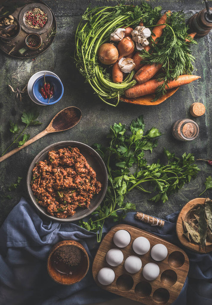 Tasty cooking. Flavored minced meat in wooden bowl with vegetables , herbs and spices ingredients, cooking spoon on dark rustic background. Top view. Home still life. Stuffing cooking preparation - Foto, Imagen
