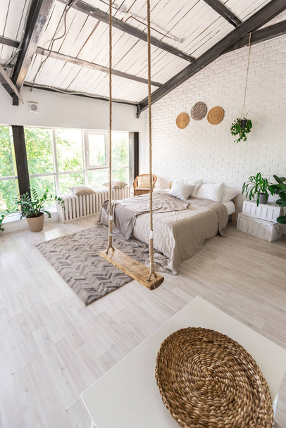 Luxury bedroom design in a rustic cottage in a minimalist style. white walls, panoramic windows, wooden elements of decoration on the ceiling, rope swings in the middle of a spacious room. - 写真・画像
