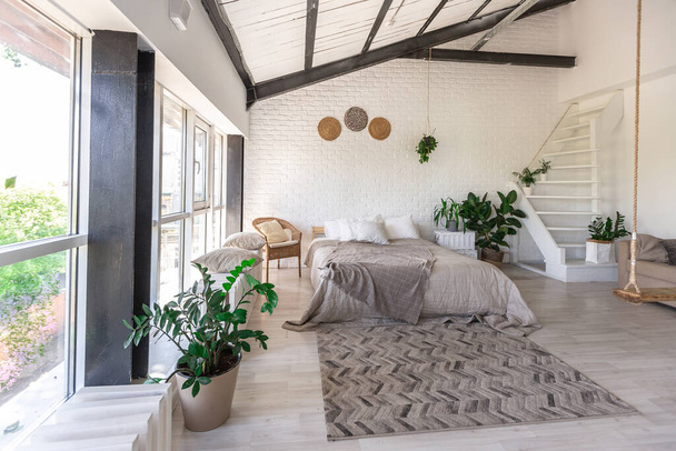 Luxury bedroom design in a rustic cottage in a minimalist style. white walls, panoramic windows, wooden elements of decoration on the ceiling, rope swings in the middle of a spacious room. - Foto, Bild