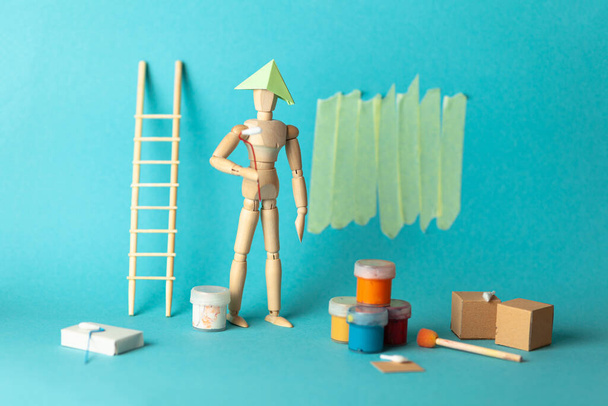 Wooden figure of man paints walls in apartment room, repair and renovation of design and decor. Paint buckets and a step ladder. DIY indoors work. - Фото, зображення