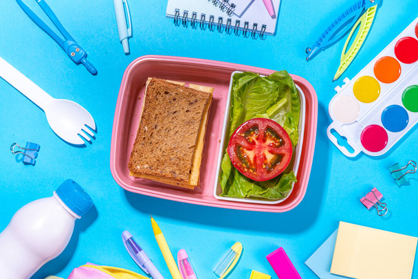 Healthy school meal, back to school concept. Children packed lunch box with balanced diet snack food - yogurt, cereal toast sandwich, apple, fresh vegetable salad, high-colored bright background - Photo, image