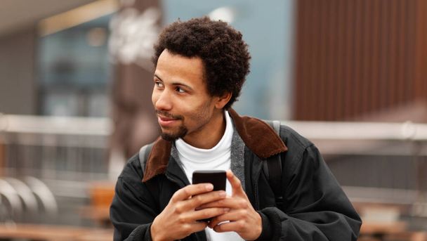 Smiling African American guy writes SMS to friends on phone. - Photo, Image