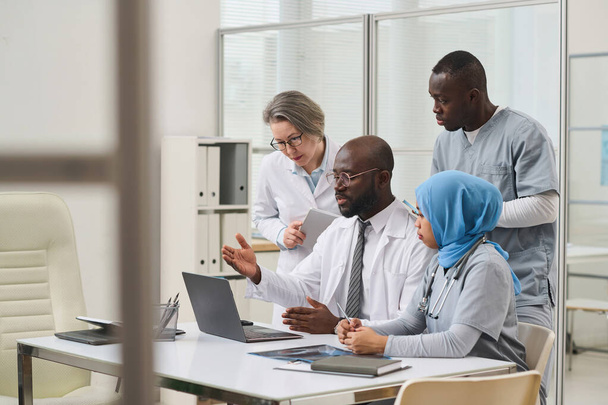 Groep van professionele artsen die laptop gebruiken in hun teamwork aan tafel tijdens zakelijke bijeenkomst in kantoor - Foto, afbeelding