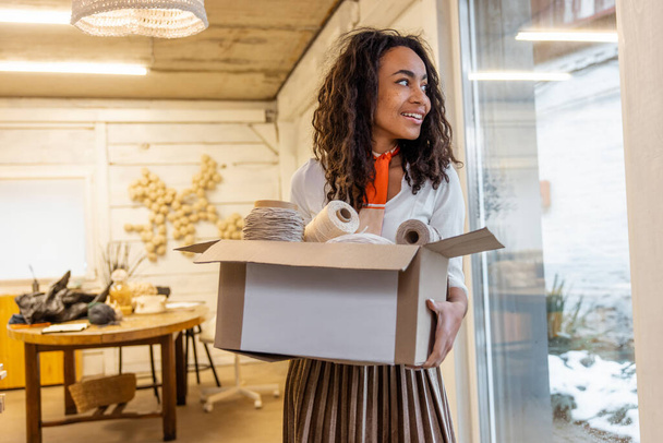 Packing boxes. Young curly-haired woman with a cardboard in hands - Foto, afbeelding