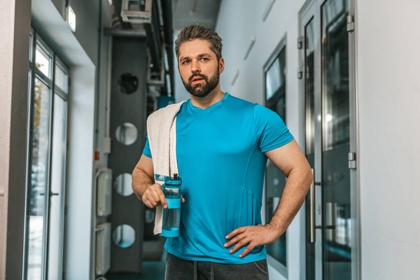 After workout. Young handsome bearded sportsman with a bottle of water - Fotó, kép