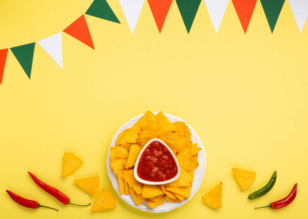 Mexikanische Fiesta mit traditionellen mexikanischen Nachos-Chips, Chilischoten und Tomaten-Salsa-Sauce auf gelbem Hintergrund. Cinco de Mayo (5. Mai) Feier Konzept. Ansicht von oben, Kopierraum. - Foto, Bild