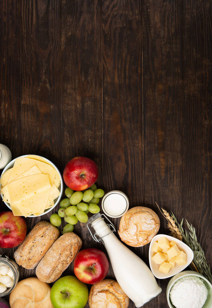 Happy Shavuot festive card. Jewish religious holiday concept. Dairy products, fruits, cheese, bread, milk bottle, cottage cheese, wheat on dark wooden background. Top view, copy space. - Photo, Image