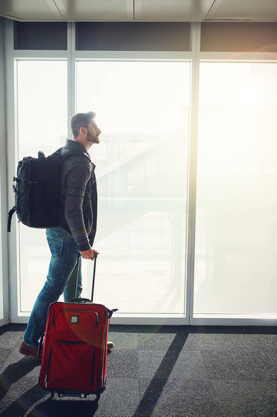 Its going to weird without her. a young man standing in an airport with luggage and looking at someone or something in front of him - Foto, imagen