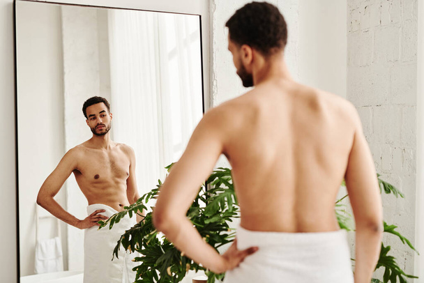 Οπίσθια όψη του νεαρού γυμνού άνδρα που κοιτάζει το μυώδες σώμα του στον καθρέφτη - Φωτογραφία, εικόνα