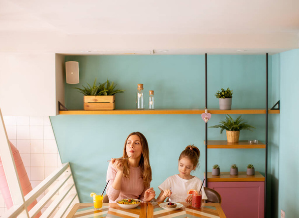 Moeder en dochter die zich vermaken tijdens het ontbijt met verse geperste sappen in het café - Foto, afbeelding