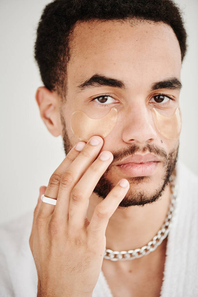 Portret van jonge metroseksuele man met accessoires aanbrengen van ooglapjes op zijn gezicht en kijken naar camera - Foto, afbeelding