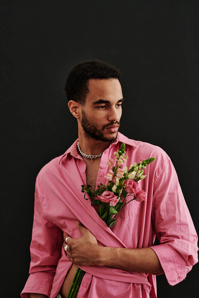 Στούντιο πλάνο του μικτού αγώνα νεαρός άνδρας ποζάρουν σε ροζ πουκάμισο με λουλούδια πάνω από το μαύρο φόντο - Φωτογραφία, εικόνα