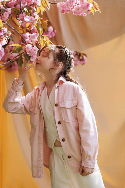 Дівчина нюхає квітучу сакуру на бежевому фоні в сонячний день
. - Фото, зображення