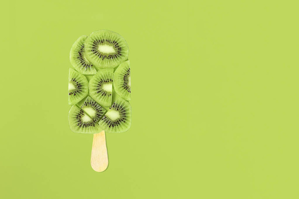 Kiwi ice cream on stick with kiwi slices on green background, copy space. - Photo, Image