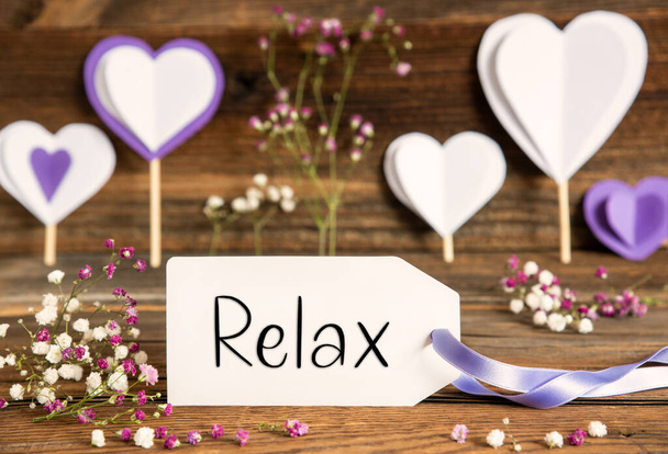 Label With English Text Relax. Purple And Lilac Decoration And Spring Flower Arrangement. Heart Symbols With Wooden Background. - Photo, Image